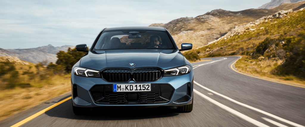 Front view of the 2025 BMW 3 Series driving on a scenic mountain road, showcasing precision engineering and sporty design, available at BMW of Northwest Arkansas.