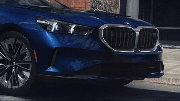 Front-end close-up of the 2025 BMW 5 Series in blue, showcasing its signature kidney grille, sleek LED headlights, and premium alloy wheels — now available at BMW of Northwest Arkansas.