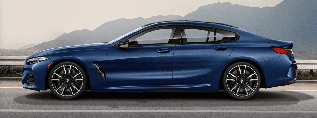 Side profile of a blue 2026 BMW 8 Series Gran Coupe parked on the road with mountains in the background.