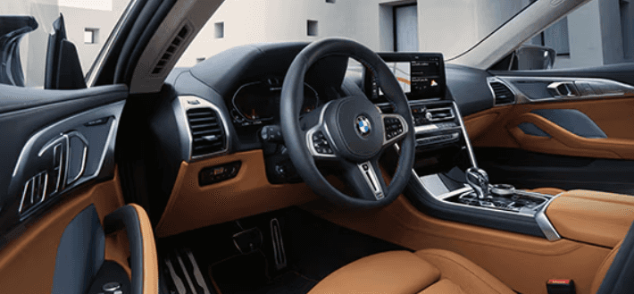 Interior view of a 2026 BMW 8 Series featuring tan leather seats, digital display, and modern steering wheel design.