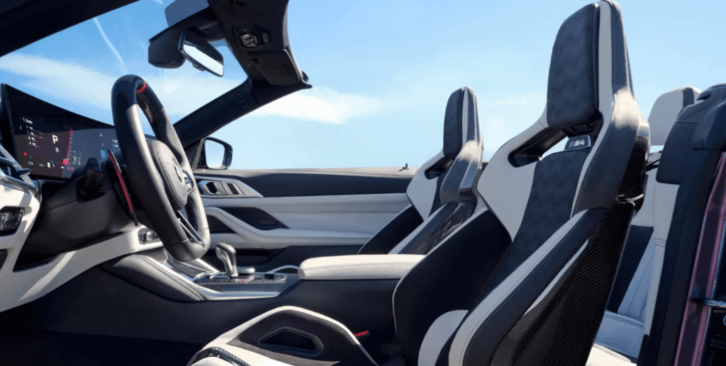 Interior of a 2026 BMW M4 Convertible with sport bucket seats and digital cockpit, shown with the top down.