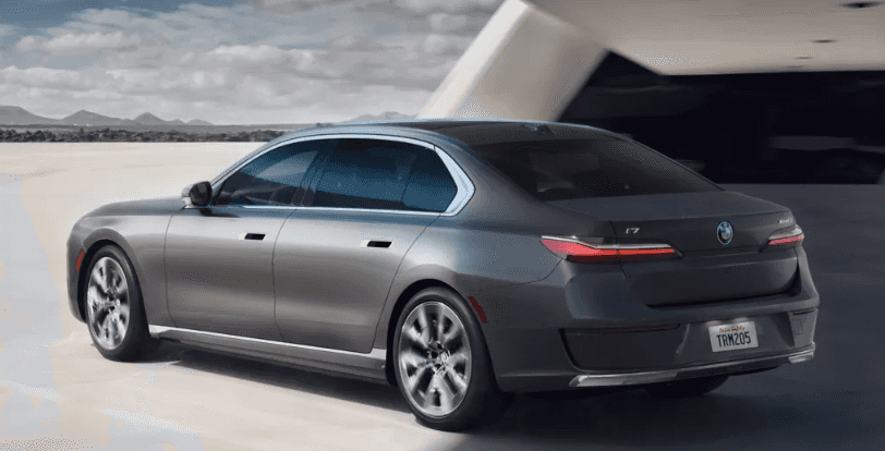 Rear and side profile of a BMW i7 driving past a sleek modern structure.