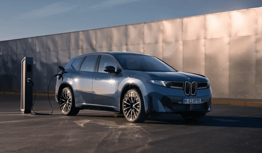2027 BMW iX3 electric SUV charging at a public station under sunlight at BMW of Northwest Arkansas