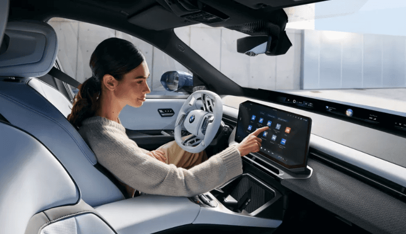 Driver interacting with the digital display inside a 2027 BMW iX3 at BMW of Northwest Arkansas
