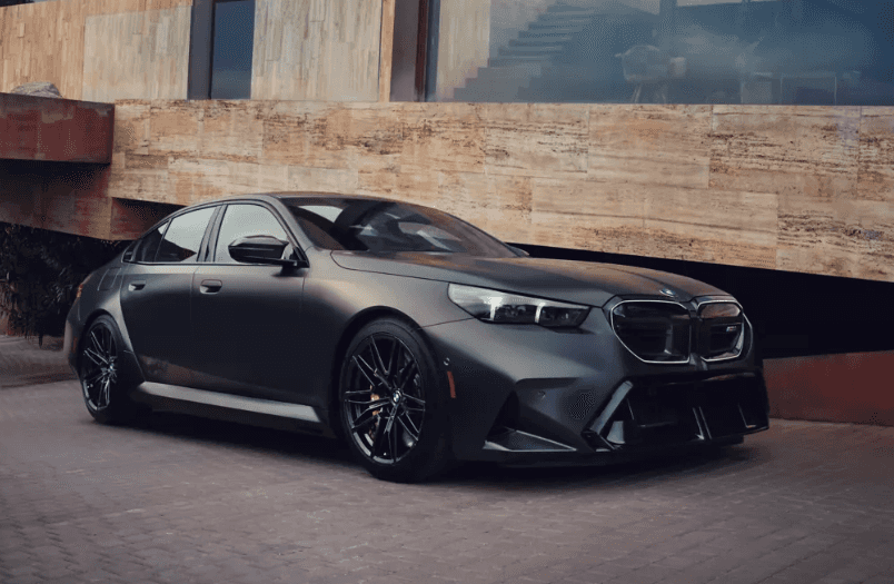 2026 BMW M5 Touring in matte black finish parked outside a modern stone building at BMW of Northwest Arkansas