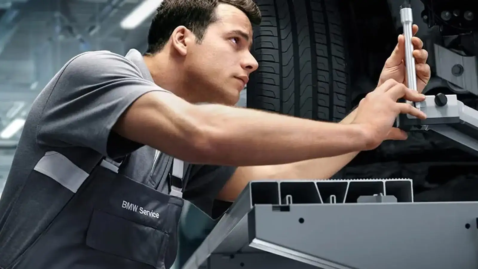 BMW Service-uniformed technician inspecting an i Series underbody — STEP-certified factory-trained service required for brake-by-wire diagnostics on the i4 and iX.