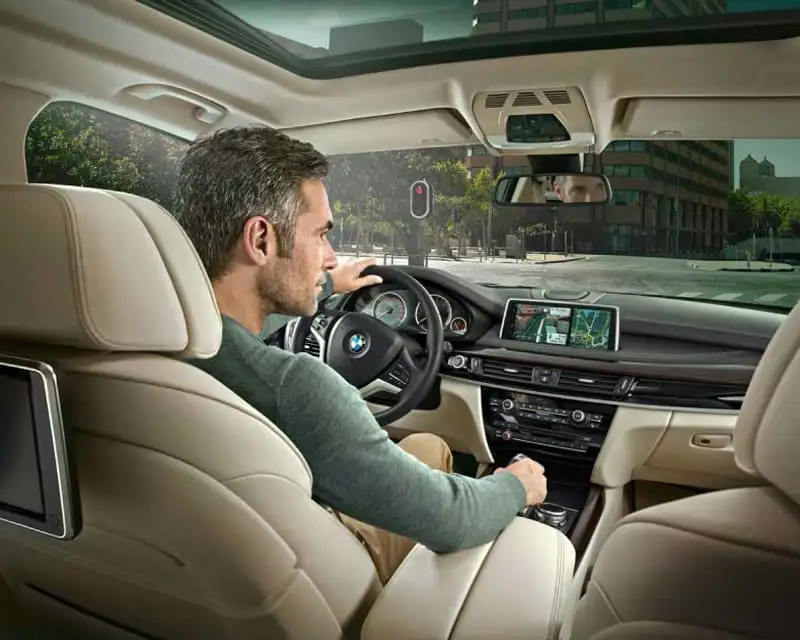 A driver behind the wheel of a BMW with navigation on the iDrive display — the ownership experience a Certified Pre-Owned BMW keeps intact