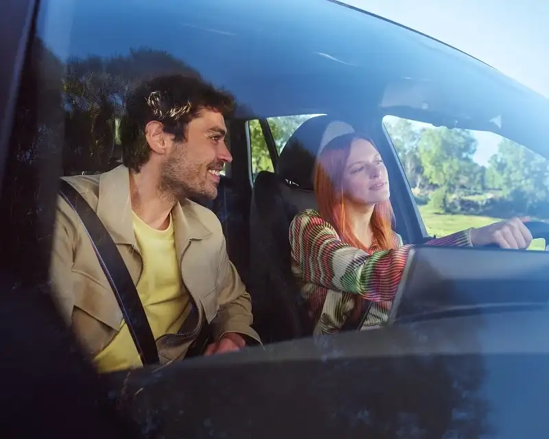 Two people riding together in a car on a sunny day — the ride that gets you to work or home while your BMW is in for service