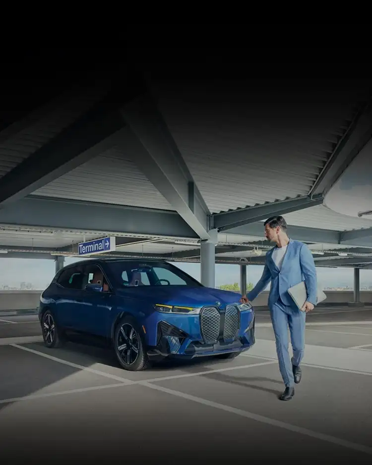 A professional walking to a blue BMW iX in an airport parking deck — the three-year, always-newest lease cycle BMW of South Atlanta sets up for Atlanta drivers