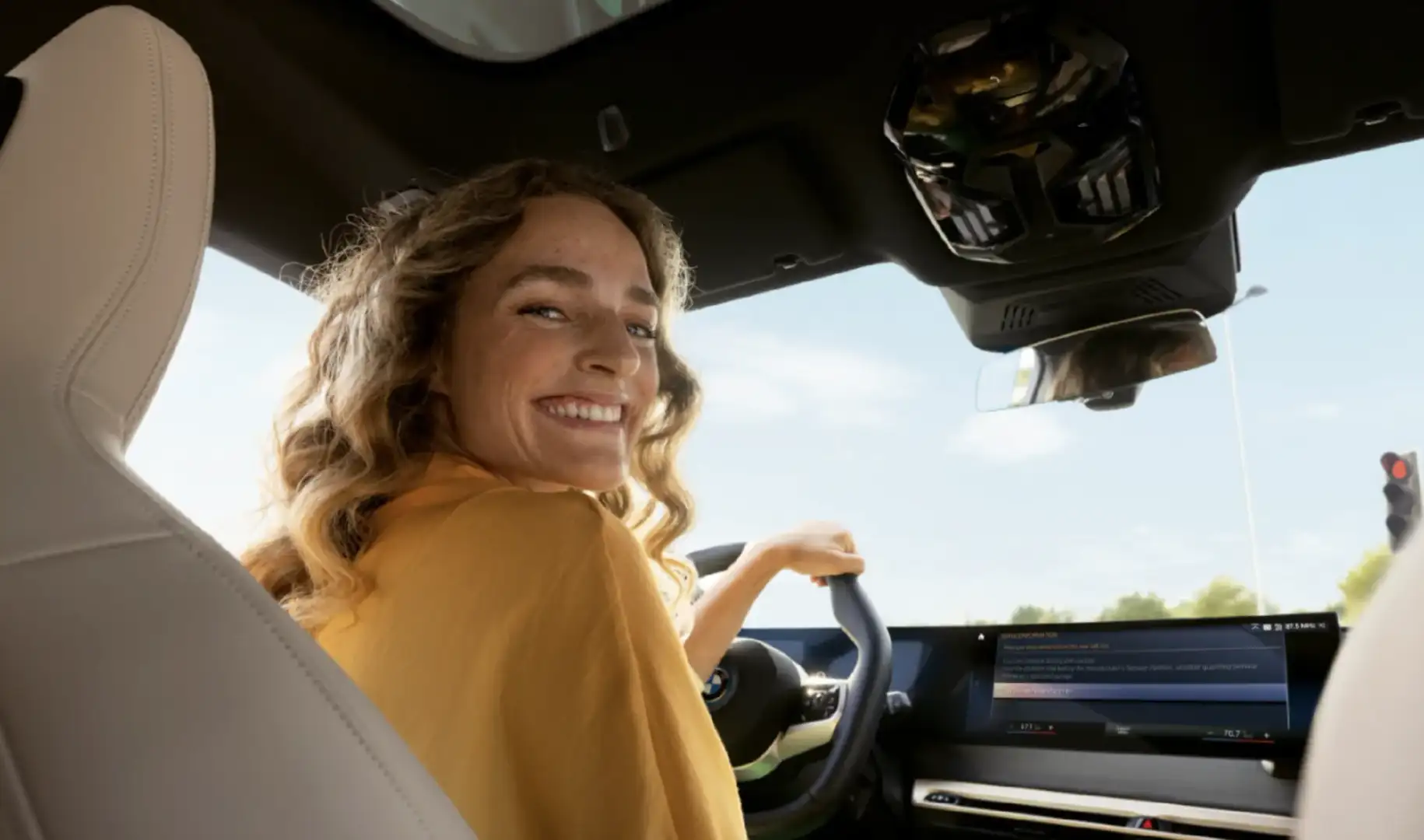 Smiling driver looking back from the front seat of a BMW with a service message on the iDrive screen
