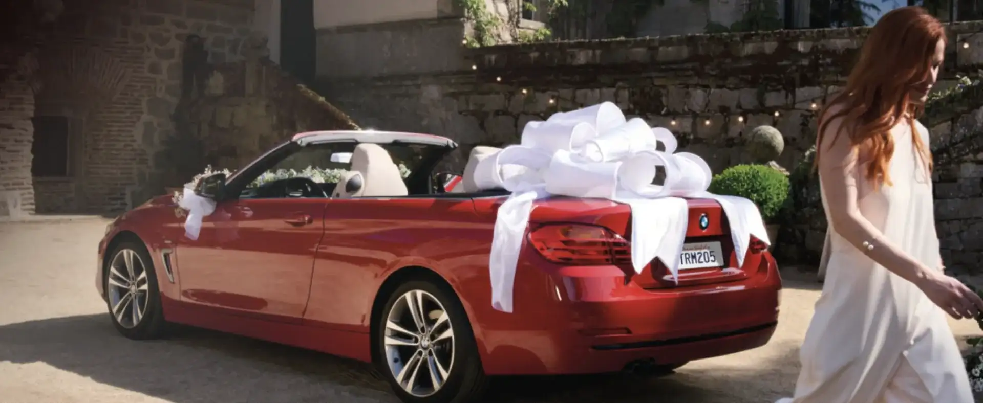 BMW convertible topped with a large white bow parked on a gravel drive