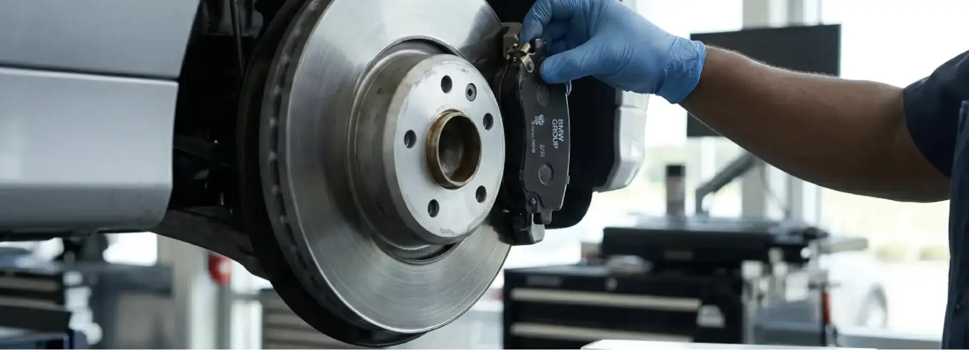A gloved technician fits a genuine BMW Group brake pad onto a car’s brake disc