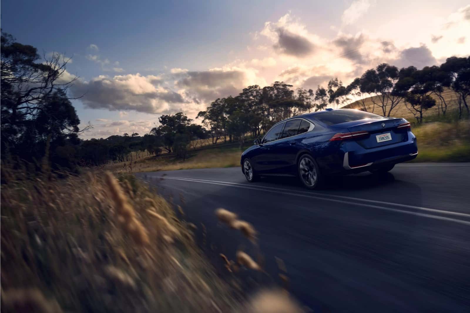 A blue BMW 5 Series driving on a country road at dusk