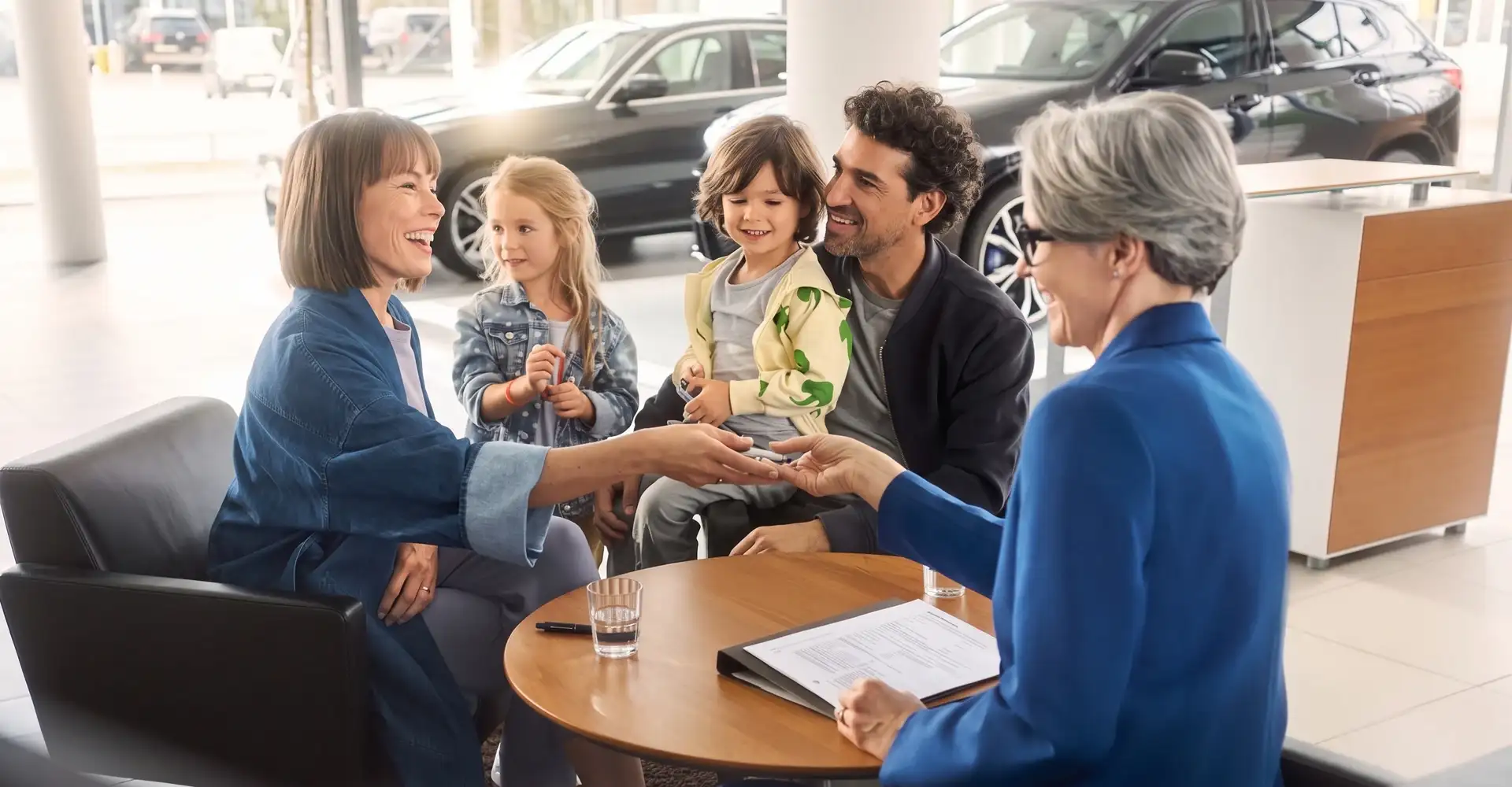 A BMW advisor handing keys to a family across a table in the showroom