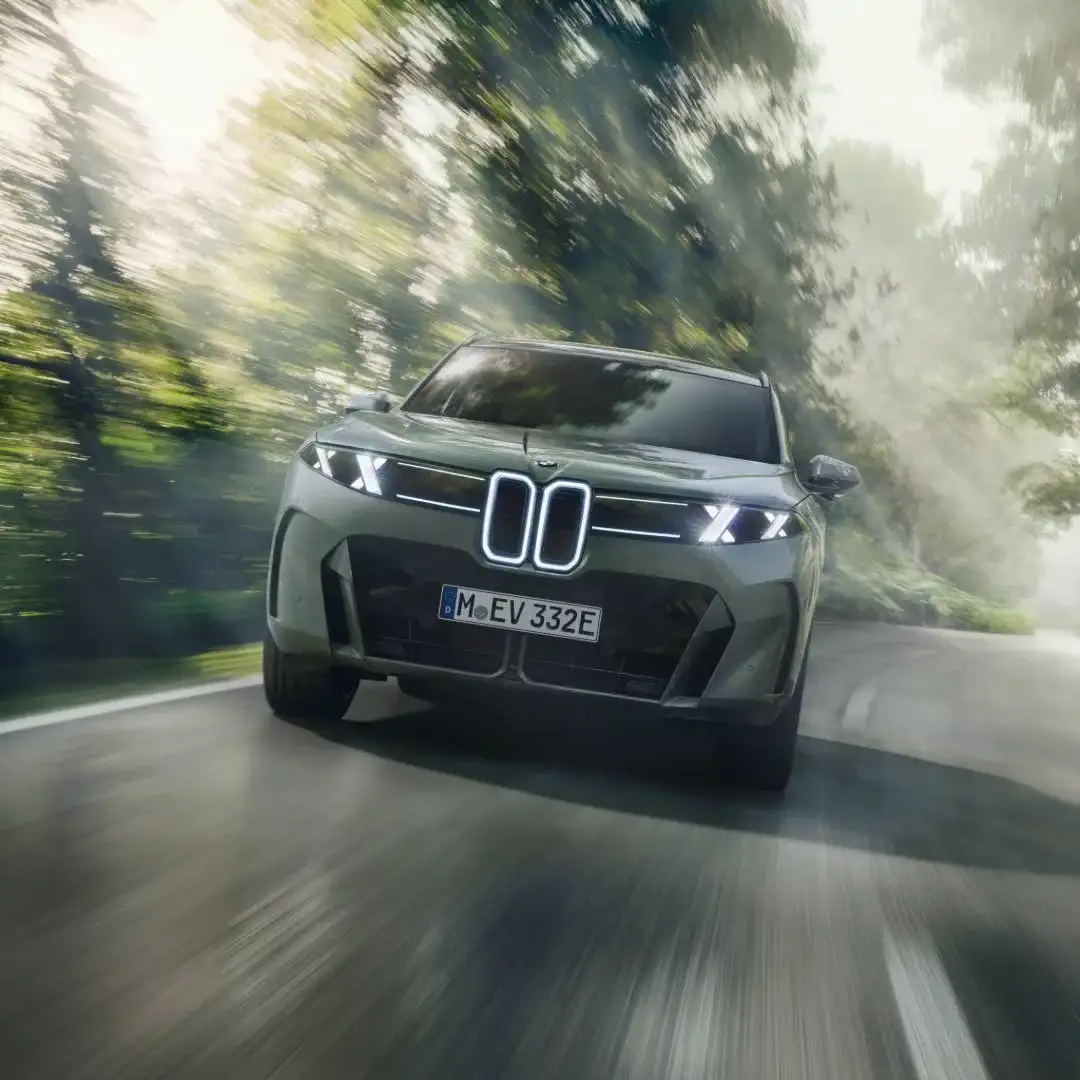 A BMW electric SUV driving towards the camera on a tree-lined road