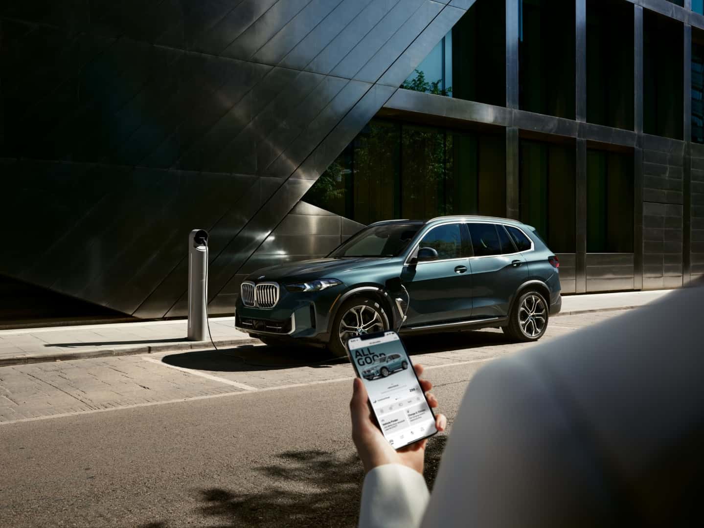 BMW X5 xDrive50e plug-in hybrid charging beside a modern building, the PHEV variant covered by this oil-change guide
