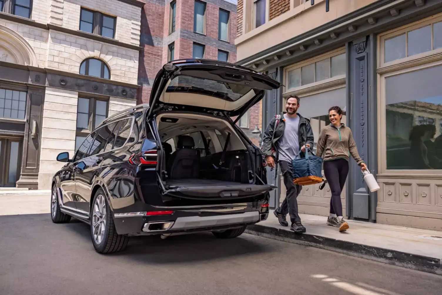 A couple loading luggage into a BMW X7 with the tailgate open