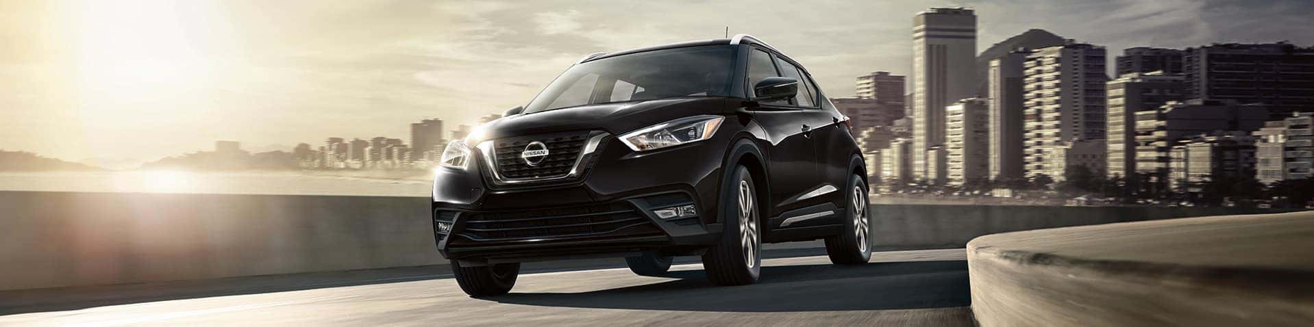 Nissan Boston is a Car Dealership near Boston MD | Black MY19 Nissan Kicks driving on highway with city in background
