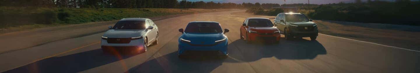 Front tracking shot of a Honda vehicle lineup driving abreast on a wide asphalt testing track at sunset.