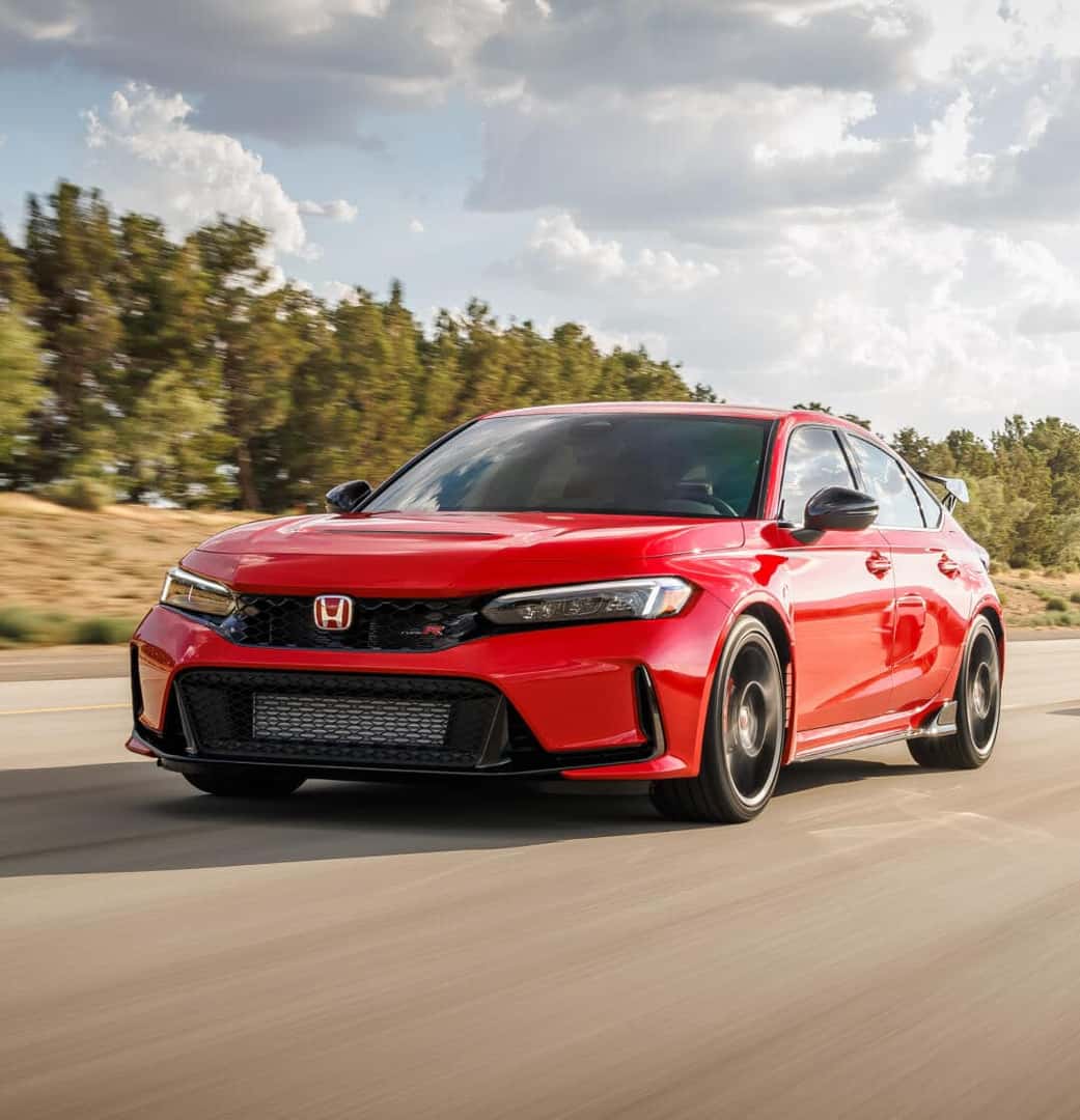 A front three-quarter action shot of a red 2023 Honda Civic R-Type driving down a sunny highway.