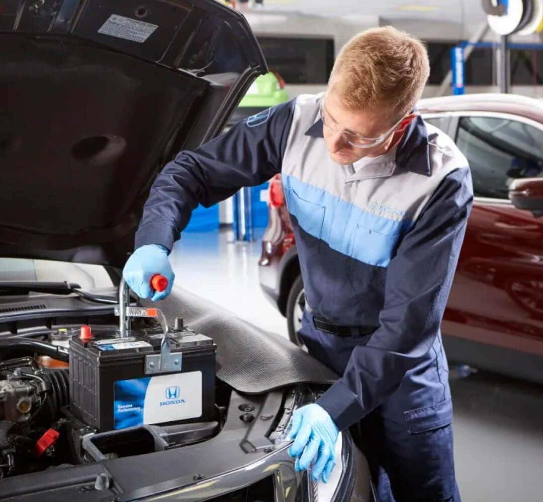 A Honda Certified Technician installs a Honda OEM battery under the hood of a car.