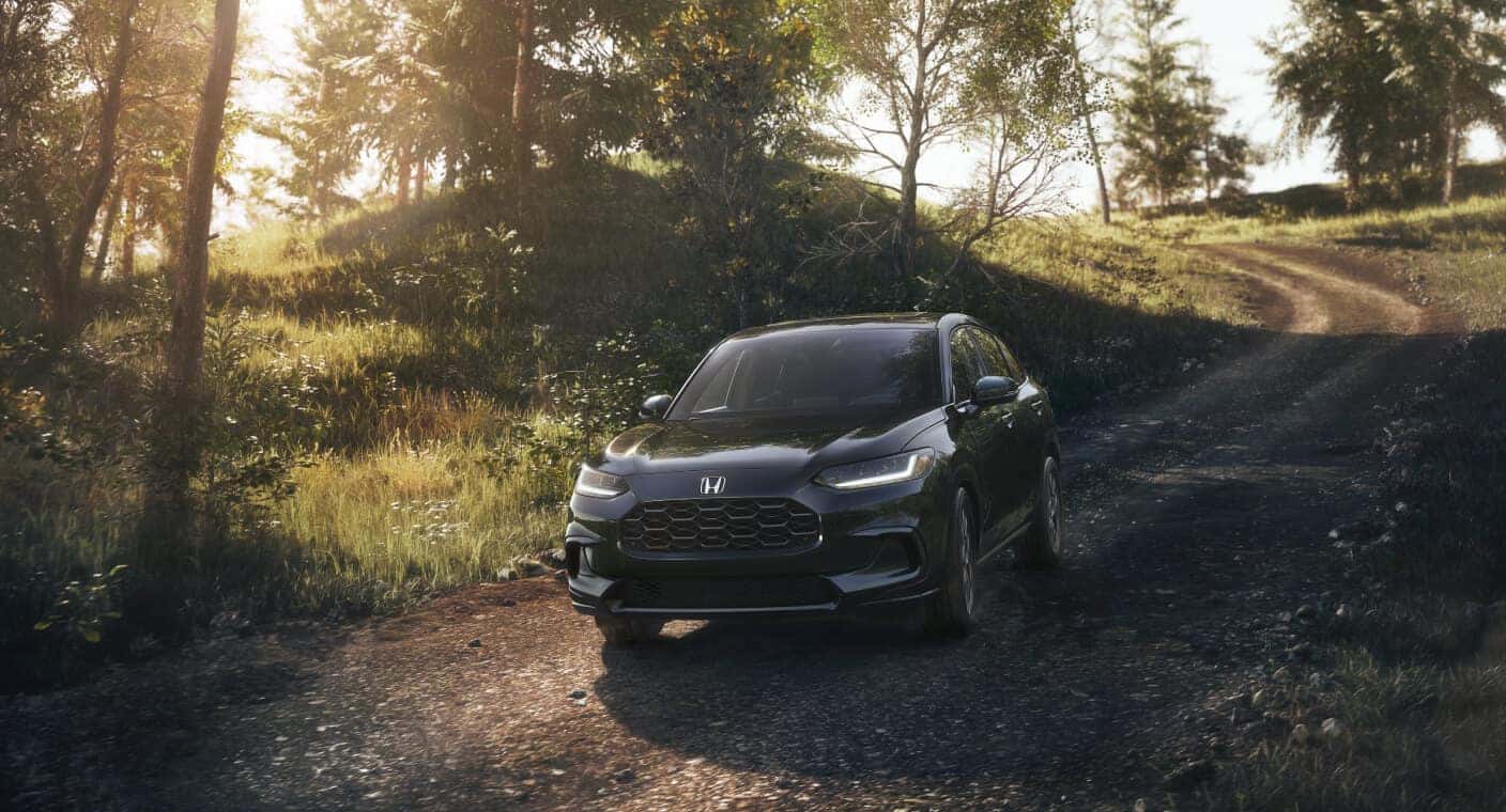 Front three-quarter view of black Honda HR-V EX-L driving on a dirt path in a sunlit forest.