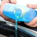 Male serviceman hands pouring blue washer fluid from a bottle into car concept