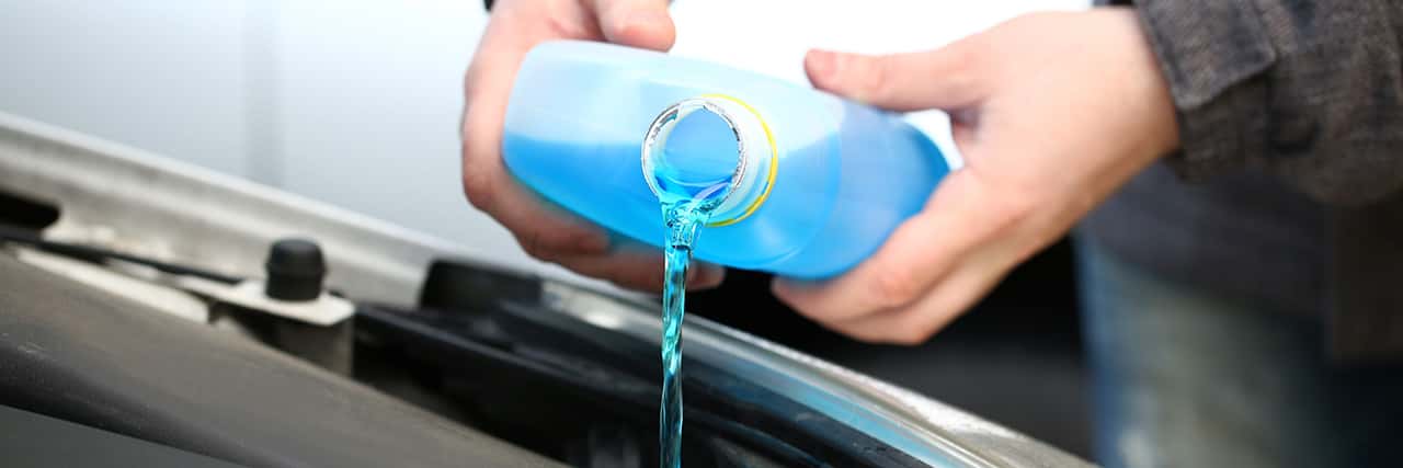 Male serviceman hands pouring blue washer fluid from a bottle into car concept