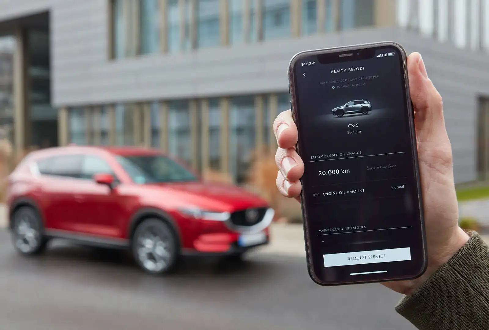 Phone showing MyMazda app in front of parked Mazda CX-5