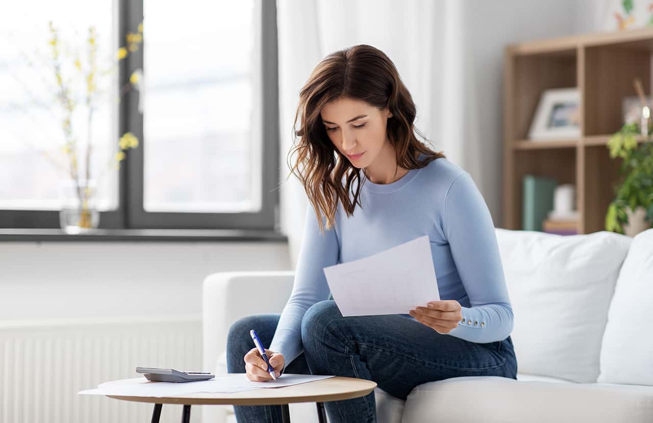 accounting, taxes and finances concept - young woman with papers and calculator at home