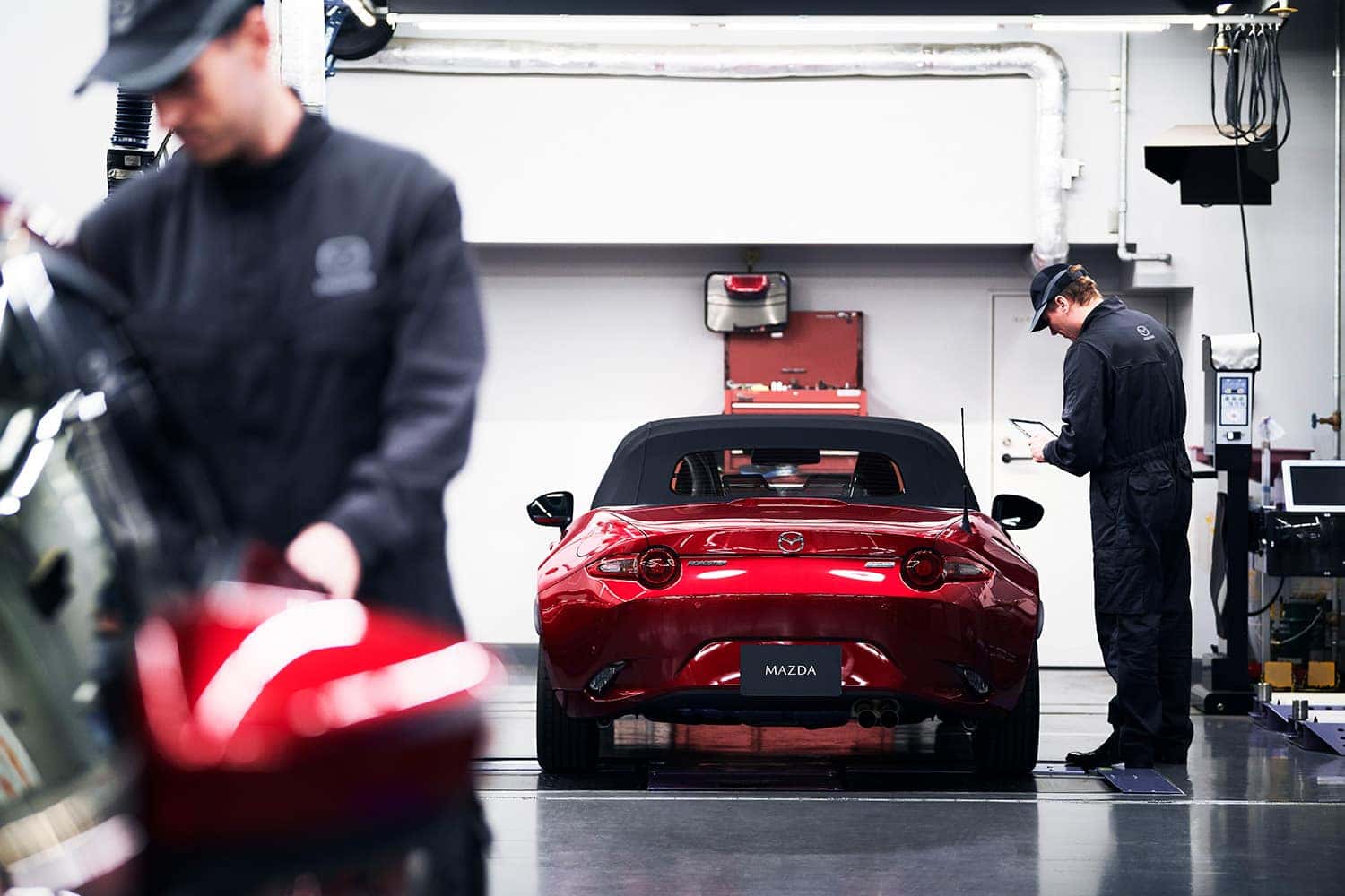 Red Mazda Miata in a Mazda service bay surrounded by technicians