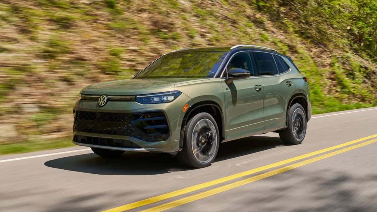 Olive Green 2026 Volkswagen Tiguan driving down road in front of hill