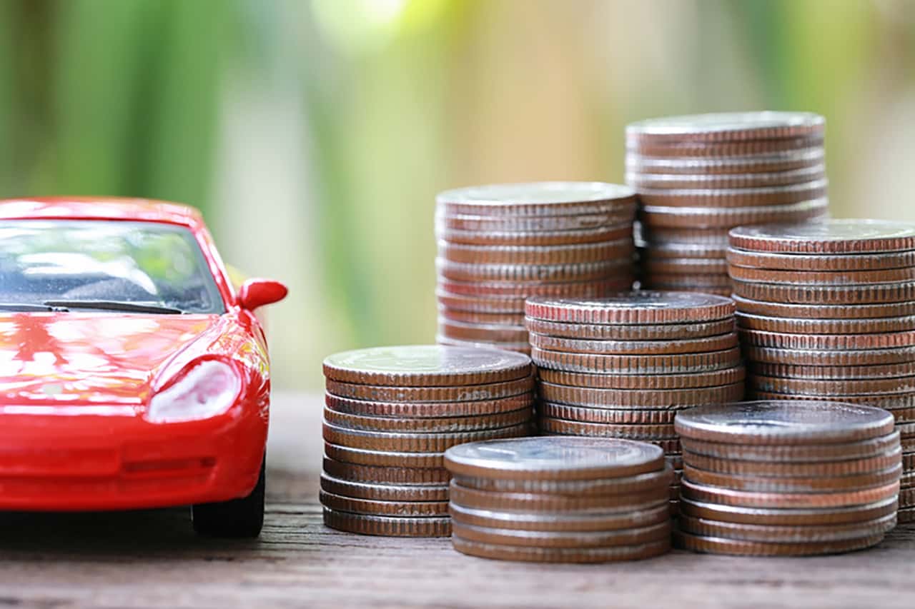 Silver coin of pile with red car model in concept savings to buy a new car or value of car and journey insurance.