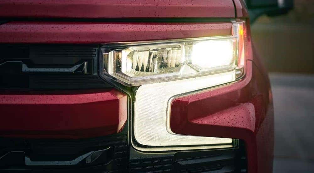 Illuminated driver side headlight on a red 2023 Chevy Silverado 1500 RST.