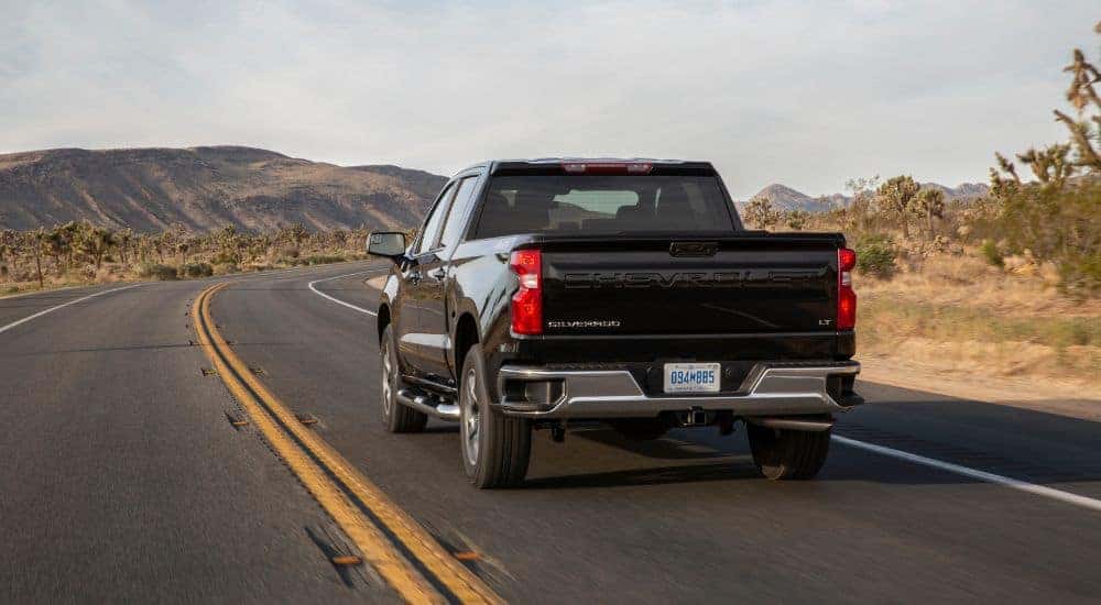 A black 2024 Chevy Silverado 1500 LT driving on an open road.