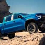 A blue 2024 Chevy Silverado 1500 for sale is off-roading on a rocky trail.