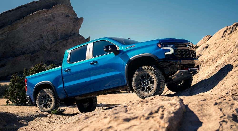 A blue 2024 Chevy Silverado 1500 for sale is off-roading on a rocky trail.