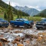 A blue 2024 Chevy Silverado High Country, a blue ZR2, and a black LT are parked off-road.