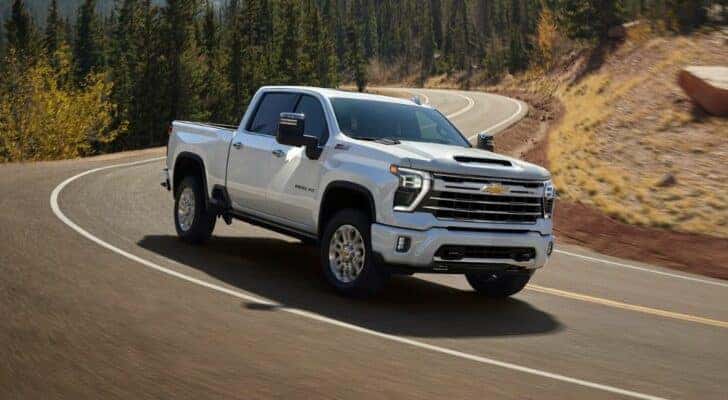 A white Chevy Silverado 2500 for sale is driving on a winding road.