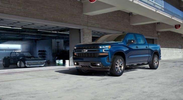 A blue 2019 Chevy Silverado 1500 is near a racecar after leaving a used Chevy dealer.