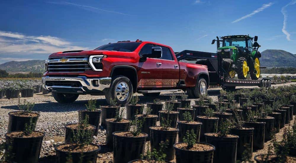 A red 2025 Chevy Silverado 3500 HD is towing a green tractor.