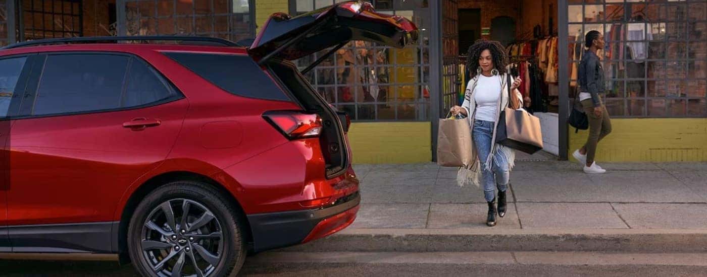 Woman walking towards the rear of a red 2024 Chevy Equinox with an open hatch.