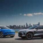 A blue 2024 Chevy Equinox EV and a grey 2024 Chevy Blazer EV parked near a city