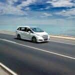 a white chrysler town and country driving on a road next to a beach