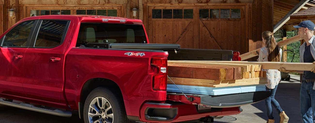 A couple is loading the bed of their red 2019 Chevy Silverado with heavy building supplies.