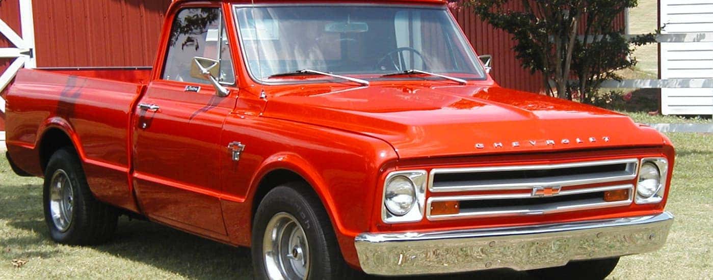 A red 1967 Chevy C/K series is parked in front of a red barn.