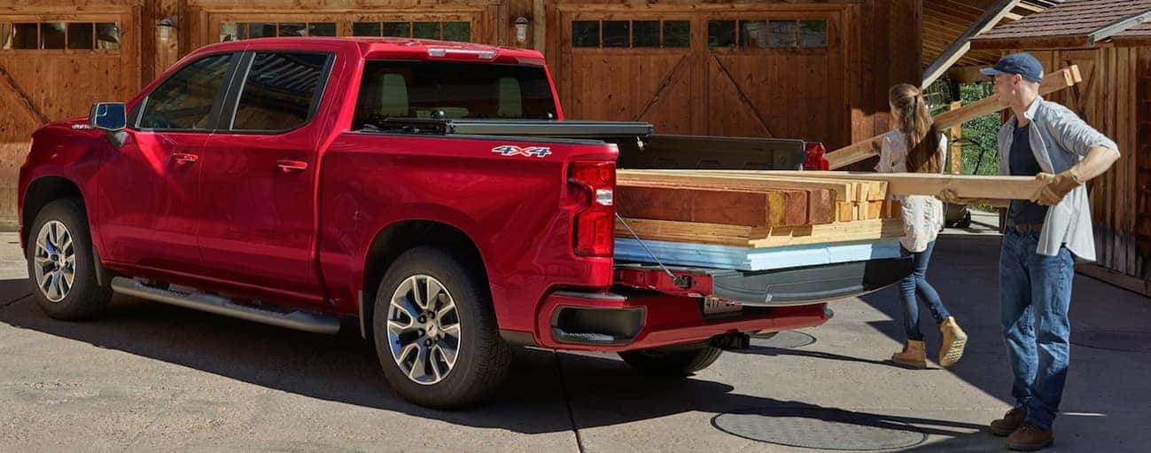 A couple is unloading pieces of wood out of their red 2020 Chevy Silverado 1500.