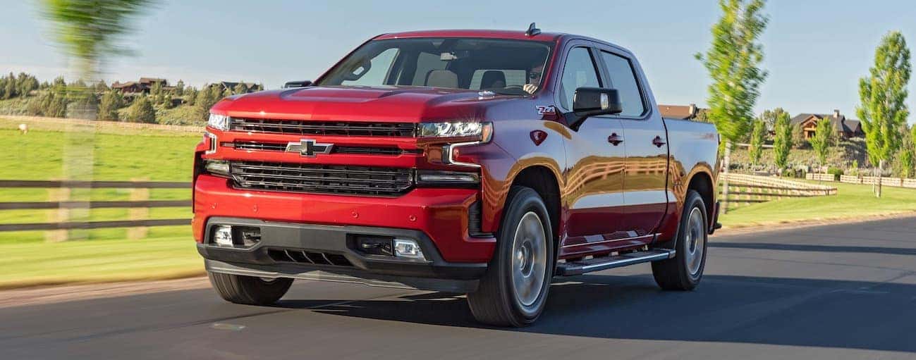 A red 2020 Chevy Silverado 1500 is driving past a grassy field that's fenced in near Bethlehem, PA. 