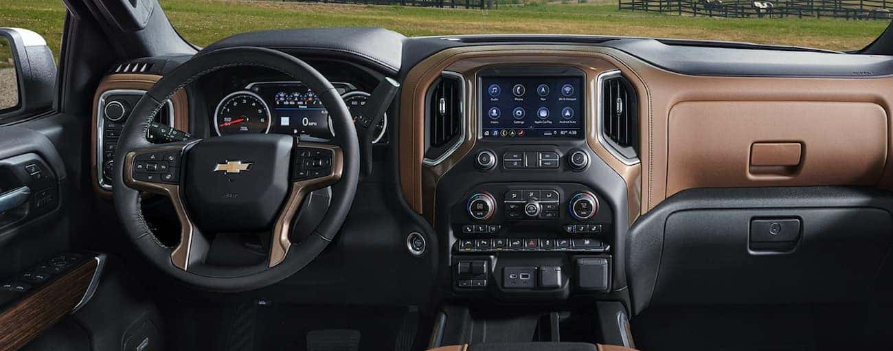 The front black and brown leather interior of the 2020 Chevy Silverado 1500 is shown with an infotainment system and drivers display. 
