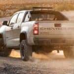 A tan 2021 Chevy Colorado ZR2, which has a factory suspension lift kit installed, is driving on a dirt road with a dust cloud rising behind it.